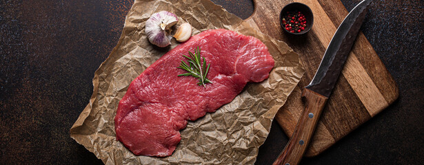 Beef lean raw fillet steak on baking paper with rosemary, garlic and spices on dark brown rustic...