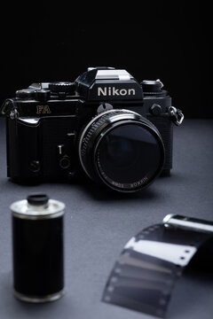 Closeup of an old Nikon FA / Nikon FE branded film camera and vintage metallic 35mm film cartridges against a dark background.