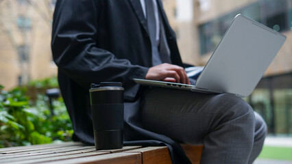 Midsection of business man sitting on bench and using laptop