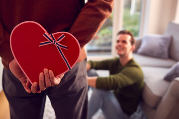 Man Surprising Same Sex Partner At Home With Heart Shaped Gift Held Behind His Back