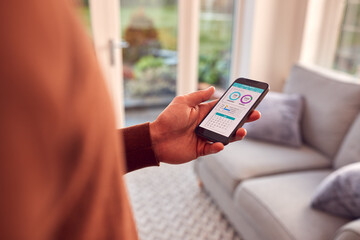 Close Up Of Man At Home Holding Phone Looking At Fitness Tracker App