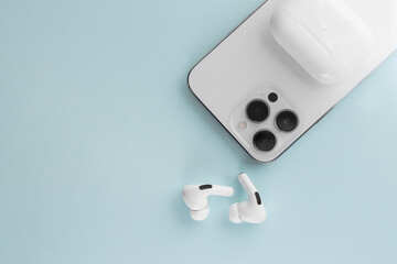 white phone with white wireless headphones on a blue background - obrazy, fototapety, plakaty