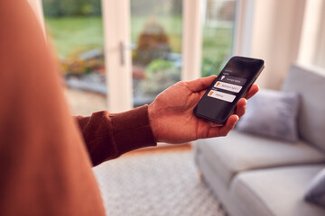 Close Up Of Man At Home Looking At App On Smart Phone To Control Lights