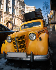 Vintage yellow car with suitcases on the roof on city street. Travel and adventure concept. Closeup.