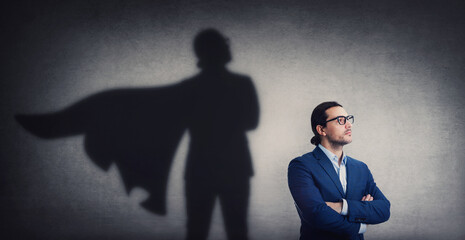 Confident businessman looking determined as casting a powerful superhero shadow on the wall. Motivated and ambitious business person shows inner strength. Hero leadership and power concept - 485848595