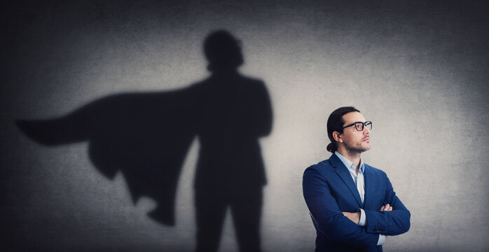 Confident businessman looking determined as casting a powerful superhero shadow on the wall. Motivated and ambitious business person shows inner strength. Hero leadership and power concept