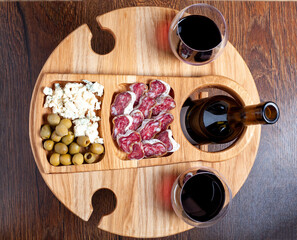 Wooden wine table with appetizers for wine top view. Wine glasses with blue cheese, fuet sausage salami and olives on wooden board. Romantic dinner at home concept.