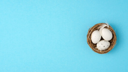 Easter eggs, feathers in a nest on a blue background. Minimal concept, top view. Copy space.