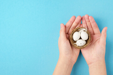 Child's hands, Easter eggs, feathers in a nest on a blue background. Minimal concept, top view.