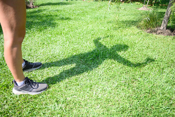 Shadow on the grass of a non recognizable caucasian woman doing strong posture with her arms.