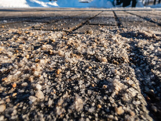 Salt grains on sidewalk surface in the winter. Applying salt to keep road clear and people safe in winter weather from ice or snow. Macro view of salt grains in sunlight in winter