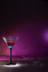 A cocktail of blue and red in a tall glass. Against the background of neon light