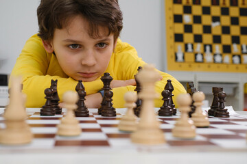 Caucasian boy playing chess. Happy concentrated child behind chess in class or school lesson....