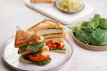 American homemade tall hot grilled cheese sandwich with tofu, cheddar, tomato slices and spinach on white scandi plate cut in triangles. Italian Tramezzini