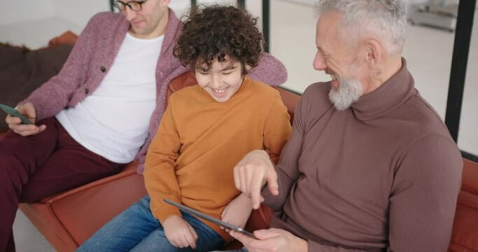 Happy gay LGBT couple looks at cute funny photos of son on tablet