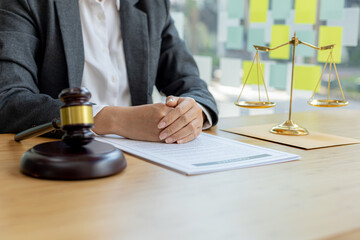 A lawyer sits in his office, on a table with a small hammer to beat the judge's desk in court. and justice scales, lawyers are drafting a contract for the client to use with the defendant to sign.