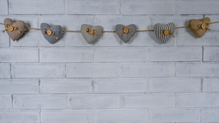 Heart-shaped figures connected by a rope hang against a white brick wall. Woven figures.