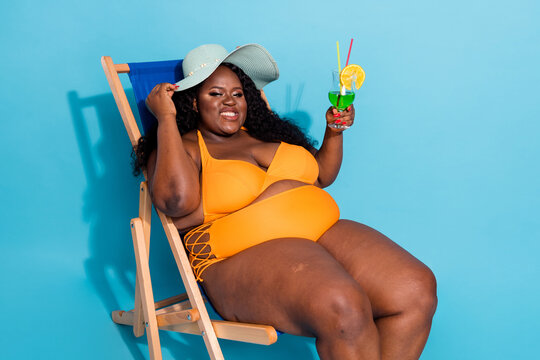 Photo of curvy obese stylish trendy big lady relax sea lie deckchair drink lemonade touch hat isolated over blue color background