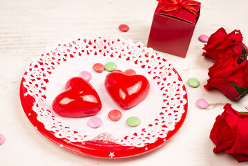 Festive concept for Valentine's Day with Appetizing icing hearts on a lacy napkin with a plate, roses and a gift box, close-up.. Table setting for a romantic meeting on Valentine's Day.