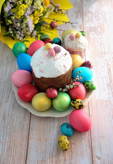 Fototapeta na wymiar Easter cakes, colorful eggs, spring flowers bouquet on table, blurred wooden background. Easter holiday concept. Festive traditional composition