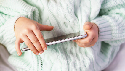 The hands of a little girl holding a mobile phone close-up. A little girl is playing a game on a smartphone.  I am interested in modern technologies. Teaching children online. Leisure at home.
