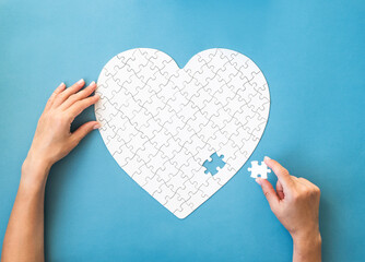 White puzzle in heart shape. Hands with white details of puzzle on blue background.