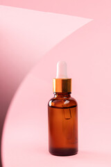 Obraz na płótnie Canvas Close up of brown glass cosmetic bottle with dropper on a pink background with abstract decor. The concept of an advertising template for beauty products