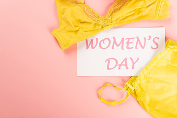 Top view of card with womens day lettering near bra on pink background