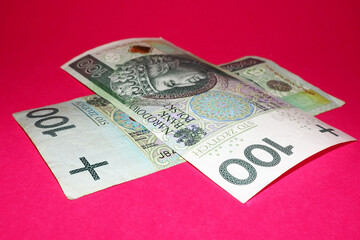 two 100 zloty bills lie on top of each other on a pink background. side view