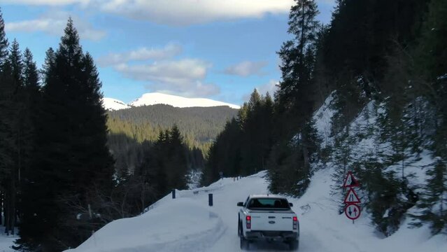 Aerial drone of a pickup truck car driving on a snowy mountain road forest during winter