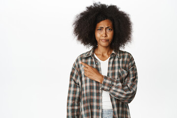 Dislike. Upset african american woman pointing left and frowning, disapprove smth, look skeptical, complaining, showing smth bad, standing over white background