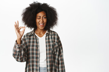 Okay, well done. Smiling african american female model shows okay, zero ok gesture in approval, agree, like and recommend smth good, white background - obrazy, fototapety, plakaty