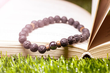 A bracelet made of black beads and a book on the grass, an amulet made of natural stones