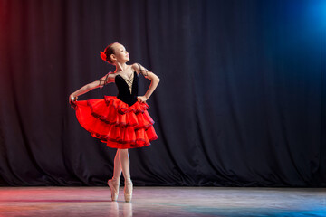 A little girl ballerina is dancing on stage in a tutu on pointe shoes with castanedas, the classic variation of Kitri.