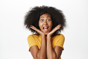 Close up portrait of enthusiastic Black woman gasping, staring amazed at camera, looking with yearning and surprise, standing over white background