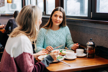 Two pretty young women talking while sitting and eating in a restaurant on a winter day.