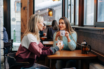 Two women drink coffee in a cozy bar and have a friendly conversation.