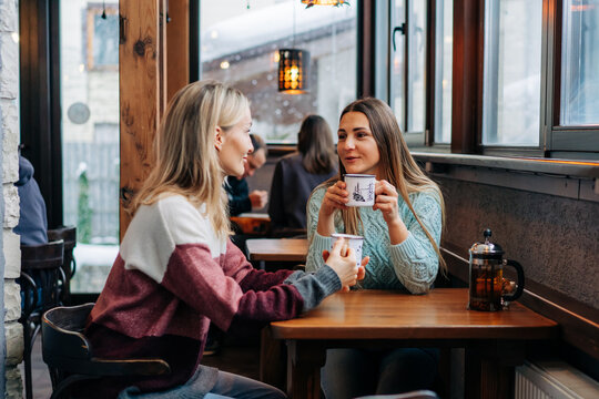 Two women drink coffee in a cozy bar and have a friendly conversation. - Powered by Adobe