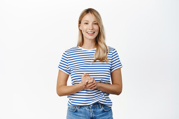 People concept. Stylish modern girl, 25 years old, standing in assistant helpful pose, ready to offer help, listening to customer and smiling, standing over white background - 485864308