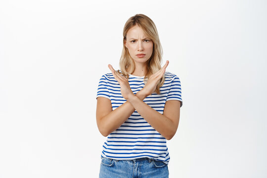 Portrait of woman showing stop sign, showing crossed arms gesture, prohibit action, rejecting smth with angry serious face, decline, saying no, standing over white background