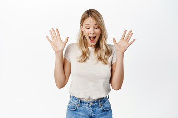 Happy smiling blond girl looking down at gift, seeing surprise and rejoicing, standing over white...