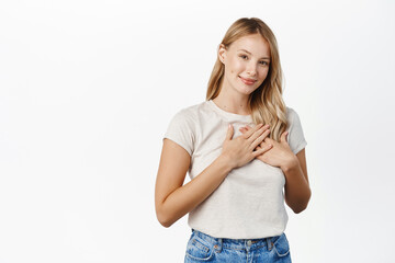 People and faces concept. Young smiling woman holding hands on heart and looking grateful, thank...