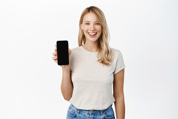 Enthusiastic smiling woman showing mobile phone screen, smartphone app interface, concept of technology and cellular, standing over white background