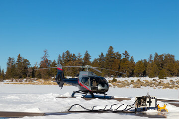 Helicopter landing on terrain full of snow and trees on a cold winter day