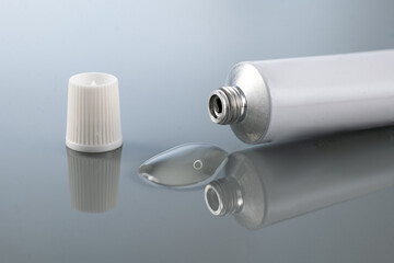 gel for external use is slightly squeezed out of the tube next to the cap on a gradient background with reflection