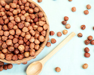 Peeled hazelnuts in a glass bowl. Near the bowl lies a wooden spoon. Healthy food concept. Flat lay