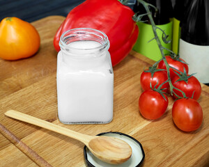 Coconut oil in a glass jar. Near the jar are sweet peppers, tomatoes and a wooden spoon. Healthy food concept