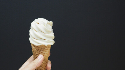 The hand is holding a soft-serve ice cream cone with a black background.