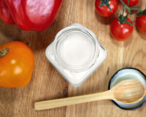 Coconut oil in a glass jar. Near the jar are sweet peppers, tomatoes and a wooden spoon. Healthy food concept. Flat lay