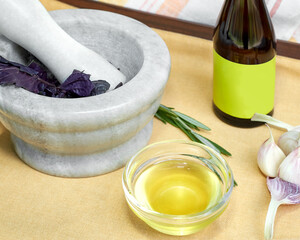 Vegetable oil in a small glass bowl. Near the bowl is a bottle of vegetable oil, garlic, a mortar for grinding with basil. Healthy food concept